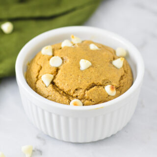 A bowl of golden brown White Chocolate Protein Blended Baked Oats, surrounded by white chocolate chips.