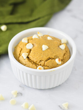 A bowl of golden brown White Chocolate Protein Blended Baked Oats, surrounded by white chocolate chips.