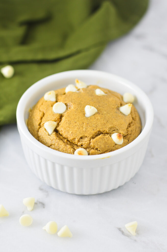 A bowl of golden brown White Chocolate Protein Blended Baked Oats, surrounded by white chocolate chips.