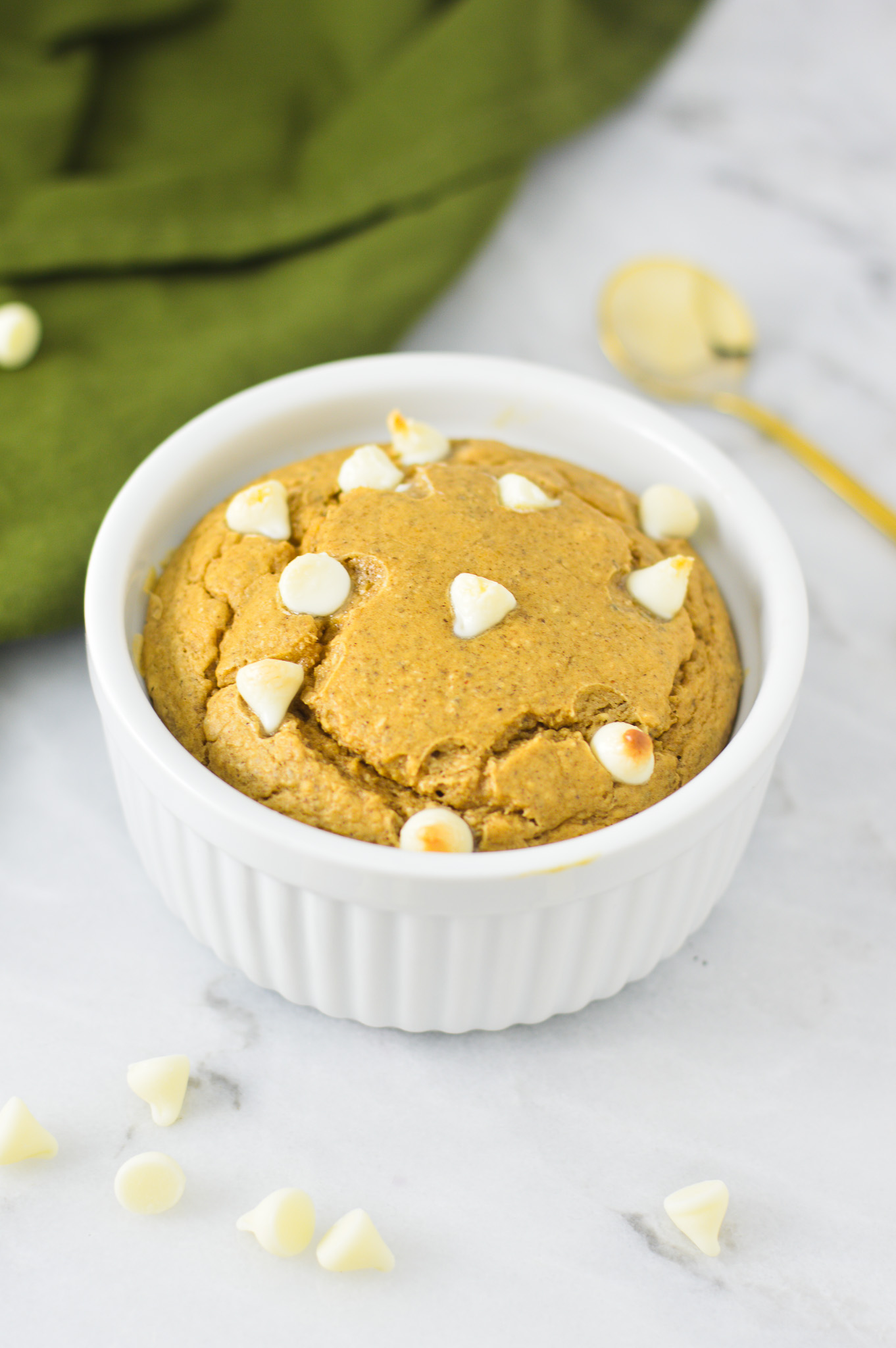 A small ramekin of White Chocolate Protein Blended Baked Oats with a small golden spoon in the background.