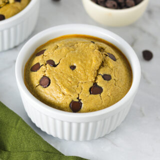 A white ramekin filled with Chocolate Chip Protein Blended Baked Oats, with some milk chocolate chips in a small bowl in the background.