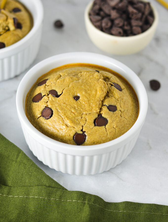 A white ramekin filled with Chocolate Chip Protein Blended Baked Oats, with some milk chocolate chips in a small bowl in the background.