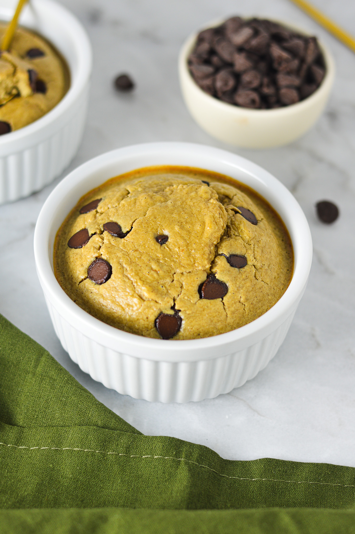 A white ramekin filled with Chocolate Chip Protein Blended Baked Oats, with some milk chocolate chips in a small bowl in the background.