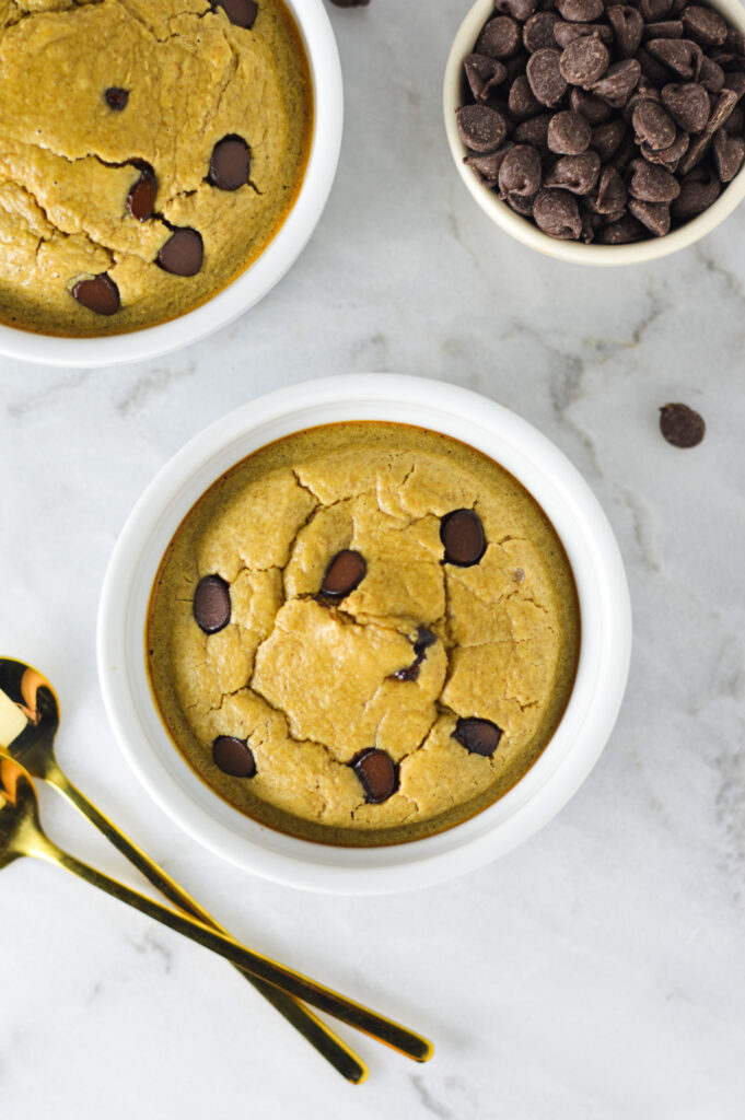 A protein packed bowl of Chocolate Chip Protein Blended Baked Oats with some small spoons and chocolate chips in the background.