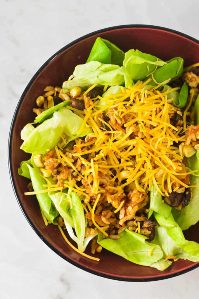 A bowl of Rice and Black Bean Salad with shredded cheese atop the crisp butter lettuce.