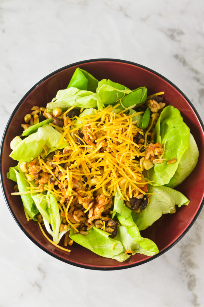 A fresh bowl of Rice and Black Bean Salad, topped with shredded cheddar cheese and black beans.