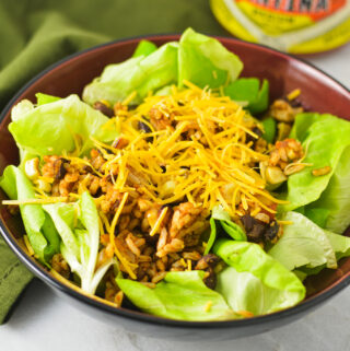 A bowl of healthy Rice and Black Bean Salad with a jar of salsa in the background.