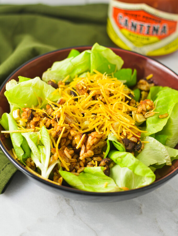 A bowl of healthy Rice and Black Bean Salad with a jar of salsa in the background.