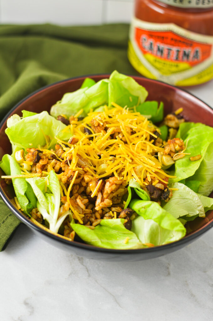 A bowl of healthy Rice and Black Bean Salad with a jar of salsa in the background.