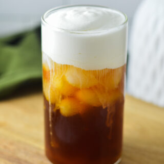 A tall glass of Sweet Cream Cold Foam on top of iced coffee. Condensation is visible on the glass, giving showing how cold this drink is.