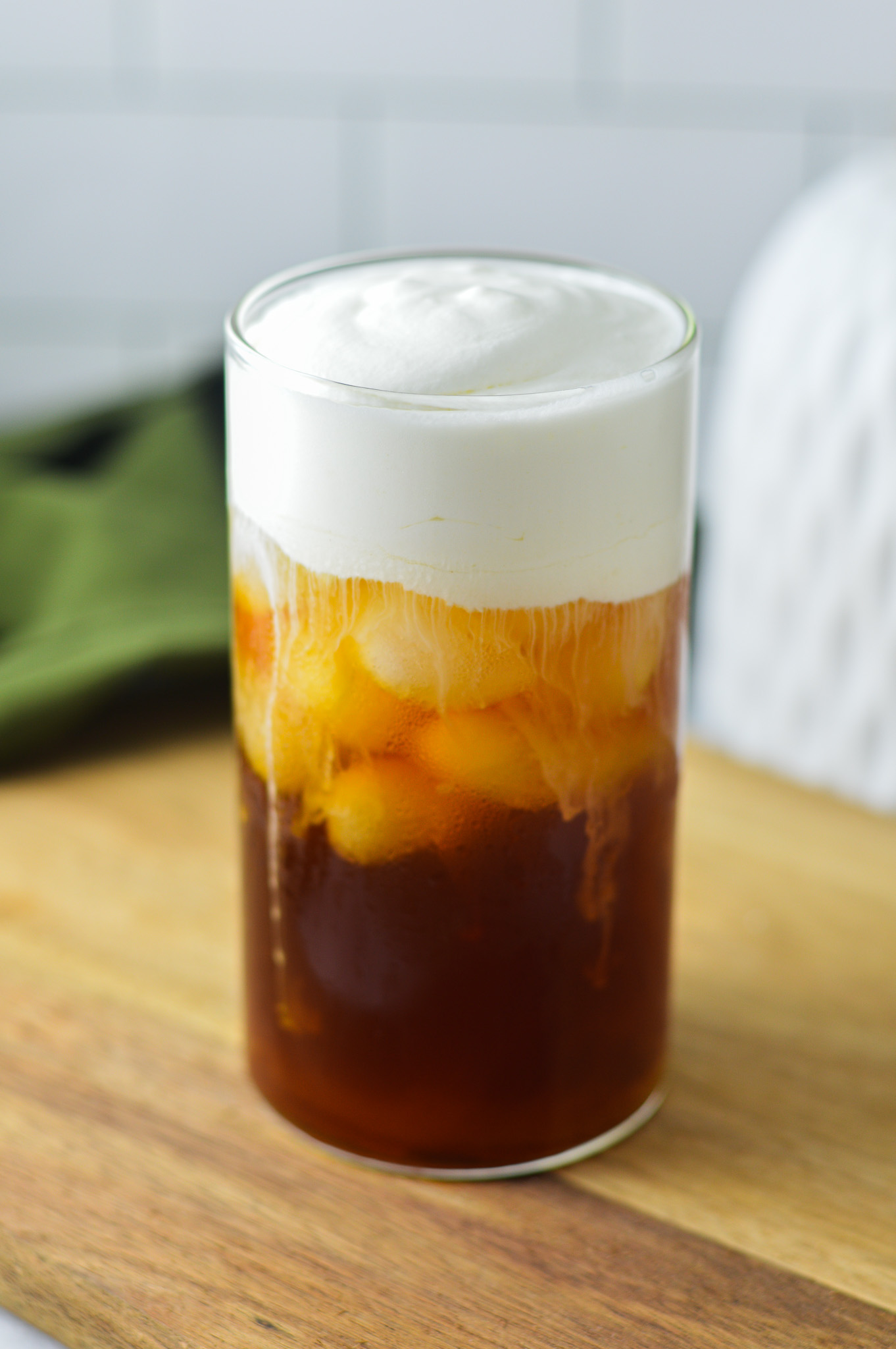 A tall glass of Sweet Cream Cold Foam on top of iced coffee. Condensation is visible on the glass, giving showing how cold this drink is.