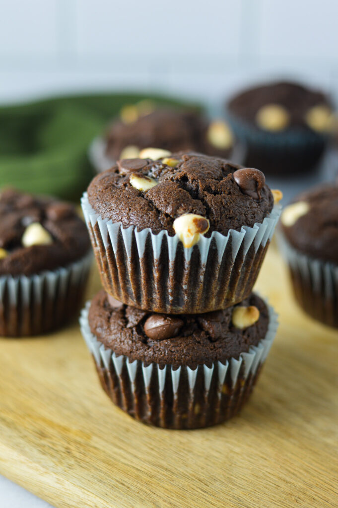 A stack of fluffy Triple Chocolate Banana Muffins, with both white and semi sweet chocolate chips covering the top of each rich muffin.