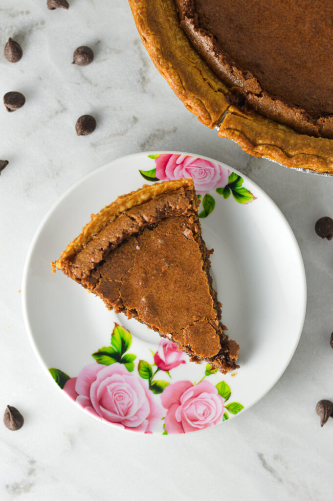 A slice of Chocolate Chess Pie, with a crackly top and chocolate chips in the background.