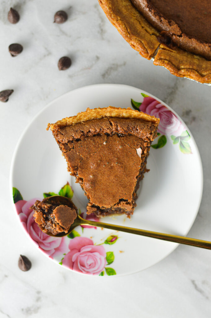 A small gold spoon taking a bite of a slice of Chocolate Chess Pie, showing the glossy top and flaky crust.