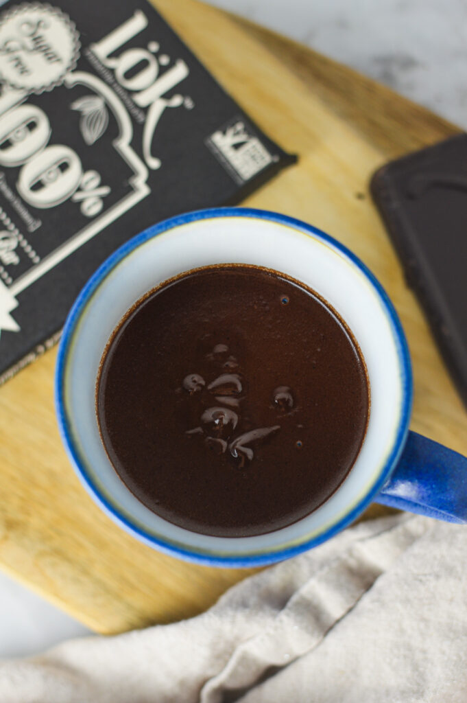 A ceramic cup full of Rich Hot Chocolate, with a pure dark chocolate bar in the background.