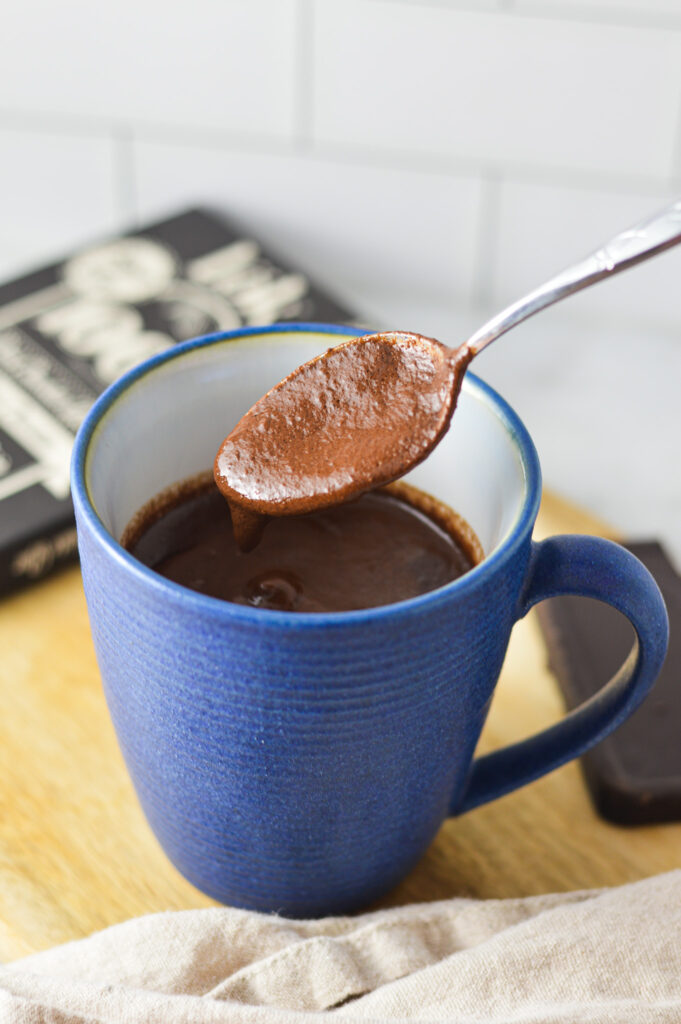 A spoon scooping some Rich Hot Chocolate from a blue mug.